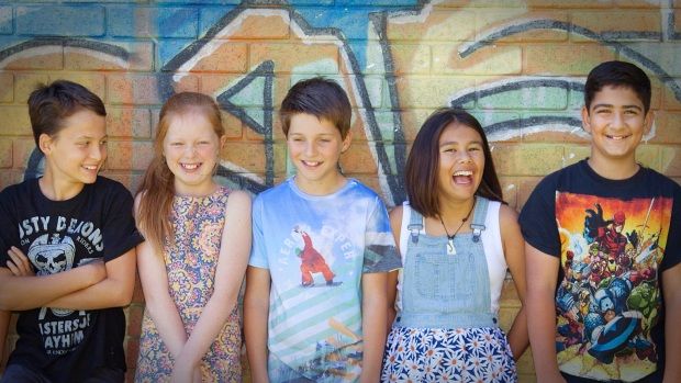 Photo of a group of school-aged kids standing in front of a wall